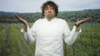 © Krakenimages.com - Man in chef uniform shrugging hands in vineyard with puzzled, raised shoulders and watch visible, rows of vines and hills behind him; uncertainty resignation.