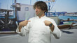 © Krakenimages.com - Hispanic man chef in white uniform holding whisk and pointing finger to chest in studio with marina backdrop and boat props; confusion doubt awkwardness.