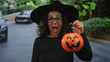 © Krakenimages.com - Middle age hispanic woman hand to face gesture holding pumpkin basket on street; surprise joy halloween playfulness.