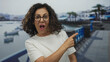 © Krakenimages.com - Middle age hispanic woman pointing finger to side and giving thumb up gesture on seaside promenade; optimism joy approval.
