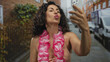 © Krakenimages.com - Middle age hispanic woman wearing bikini and lei holding smartphone for video call on street; celebration relaxation.