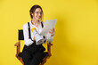 © New Africa - Professional film director with megaphone and script on chair against yellow background. Space for text