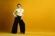 © New Africa - Beautiful young woman with piercings in wide pants in color light on yellow background. Space for text