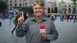 © Krakenimages.com - Man reporter holding news microphone and pointing index finger in street; confidence optimism warmth engagement.