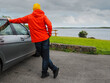 © mark_gusev - A tourist man in red jacket is standing by a car with picturesque lake in the background. The sky is cloudy and the water is calm. Travel and tourism. Calm and relaxing mood.