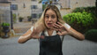 © Krakenimages.com - Woman with hands on chest and fingers splayed in building courtyard, denim apron and white short sleeve tee visible; surprise sincerity.