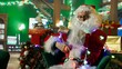 © DC Studio - Santa Claus entangled in led lights while adorning workshop for Christmas, preparing it for families visiting. Costumed man knotted in xmas lights while doing holiday season decorations, camera A