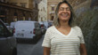 © Krakenimages.com - Woman wearing glasses and striped v neck t shirt smiling with eyes closed beside a white van on a narrow cobblestone street with stone buildings; contentment travel memory.