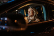 © Zamrznuti tonovi - Woman driving car at night in cityscape, smiling, enjoying evening commute and urban lifestyle