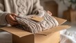 © Neuroworld - A young woman with long brown hair ties a tag to a neatly wrapped secondhand sweater. Boxes are visible in the background, emphasizing the concept of recommerce.