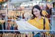 © Laingzaifa - An Asian woman is happily browsing for fashionable clothes in a boutique, smiling as she shops, holding shopping bags, showcasing the enjoyment of modern shopping.