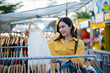 © Laingzaifa - An Asian woman is happily browsing for fashionable clothes in a boutique, smiling as she shops, holding shopping bags, showcasing the enjoyment of modern shopping.