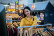 © Laingzaifa - An Asian woman is happily browsing for fashionable clothes in a boutique, smiling as she shops, holding shopping bags, showcasing the enjoyment of modern shopping.