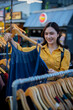 © Laingzaifa - An Asian woman is happily browsing for fashionable clothes in a boutique, smiling as she shops, holding shopping bags, showcasing the enjoyment of modern shopping.