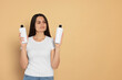 © Aashir - Beautiful young woman holding bottles of shampoo on beige background, space for text