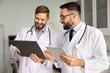 © fizkes - Interaction and sharing knowledge in hospital. Friendly smiling male doctors coworkers in uniform solve scientific problem discuss diagnosis exchange information using paper notes electronic documents