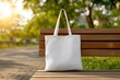 © VictorCanalesStudio - with copy space White canvas tote bag resting on a wooden bench in a park during sunny weather