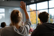 © EricMiguel - High school female student raises hand in sunlit classroom — blonde hair in messy bun, gray hoodie, seated beside male classmate by large window
