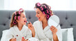 © Стивен Щиров - Mother and daughter applying lipstick together while sitting on a bed with hair rollers