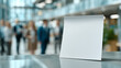 © pattozher - Blank Canvas in Modern Office: A pristine, blank note stands prominently on a sleek, modern desk, the blurred backdrop of a bustling office suggesting potential, messages, and communication.
