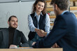 © opolja - Happy businessman and businesswoman shaking hands at group board meeting. Professional business leaders making handshake agreement