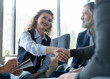 © opolja - Happy businessman and businesswoman shaking hands at group board meeting. Professional business leaders making handshake agreement