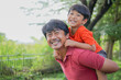© tuan12 - Smiling man giving a piggyback ride to a happy young boy outdoors, joyful family bonding, positive parenting and quality time concept.