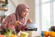 © Art_Photo - Happy young asian muslim woman in hijab smelling aroma of hot soup while cooking in kitchen, Islamic housewife preparing delicious halal meal, Ramadan Iftar, food scent and healthy lifestyle concept