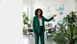 © GodNopparat - Business Presentation: A confident woman in a vibrant green suit stands in a modern office, presenting data with a friendly smile, surrounded by thriving plants.