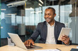 © Liubomir - Happy mature business executive working on a computer and holding a tablet, managing tasks at his modern office desk, feeling successful and connected to global business