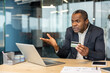 © Liubomir - Mature businessman sitting at an office desk, holding a credit card and expressing frustration while looking at a laptop, encountering financial transaction issues during online shopping or banking