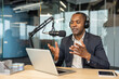 © Liubomir - Adult man wearing headphones and using a laptop while actively gesturing and speaking into a professional microphone, broadcasting from a modern studio