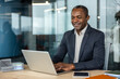 © Liubomir - Experienced professional man actively smiling while typing on a laptop and concentrating on his work at a light wooden desk ,in a contemporary corporate office environment