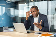 © Liubomir - Mature businessman experiencing stress and frustration, holding hand to head, looking overwhelmed by a problem on his laptop while working in a modern office