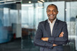 © Liubomir - Confident mature businessman posing with a friendly smile and arms crossed, standing in a contemporary corporate environment, projecting success and leadership