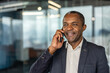 © Liubomir - Confident mature professional man communicating cheerfully on a mobile phone, representing success, connection, and technology in a corporate environment