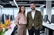 © Alex & M Studio - successful professional business partners man and woman standing together in modern white office space with colorful flower accent in foreground workspace