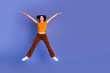 © deagreez - Young girl jumps with arms outstretched against violet background wearing orange top brown pants white sneakers