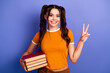 © deagreez - Young female student holds books smiles and shows peace sign against blue background