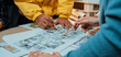 © InfiniteFlow - A group of professionals engage in a creative meeting, closely analyzing detailed architectural floor plans and sketches on a collaborative workspace table. SACTR