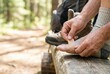 © Stitch - Hiker sitting on a log applies a bandage to a blister on his foot during a forest trek.