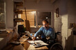 © Davor - Middle-aged man in wheelchair working at home office with laptop and cat
