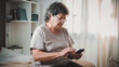 © Emanuel - Relaxed mature old 80s woman, older middle aged female customer holding smartphone using mobile app, texting message, search ecommerce offers on cell phone technology device sitting on couch at home.