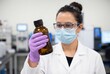 © Meow Creations - Female scientist in a mask holding a glass bottle in a laboratory