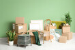 © Pixel-Shot - Packed chair, houseplants and cardboard boxes near green wall. Moving house concept
