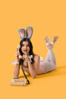 © Pixel-Shot - Sexy young woman in bunny costume with telephone showing silence gesture on yellow background. Easter celebration