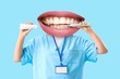 © Pixel-Shot - Female dentist with mouth instead of head holding tooth brush and paste on light blue background