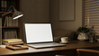 © bongkarn - White screen laptop with books and coffee on wooden table under lamp light in dim study office room.
