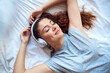 © Westend61 - Portrait of happy young woman with eyes closed lying on bed listening music with headphones