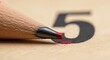 © Meera Graphic  - Close-up of sharpened pencil tip with red paint on wooden surface with number 5
